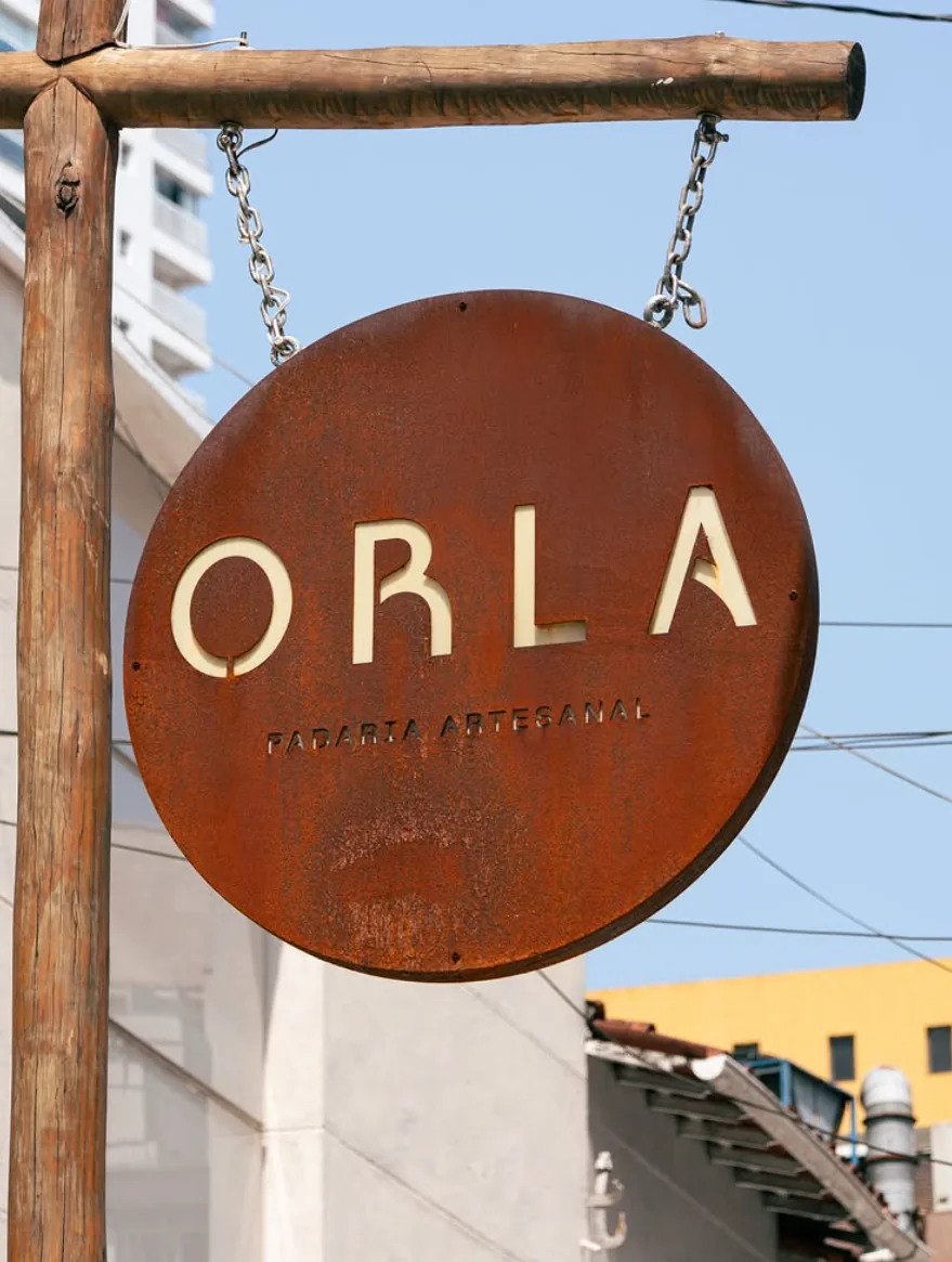 Placa circular de madeira com o nome ORLA na fachada